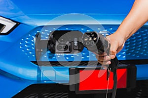 Man holding power supply cable at electric vehicle charging station.