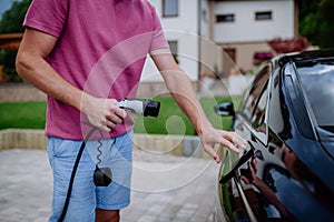 Man holding power supply cable at electric vehicle charging station.