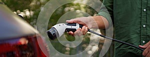 Man holding power supply cable at electric vehicle charging station, closeup