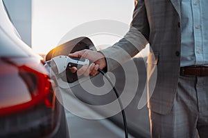 Man holding power supply cable at electric vehicle charging station, closeup