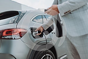 Man holding power supply cable at electric vehicle charging station, closeup