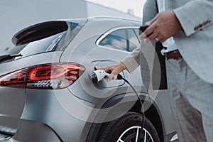 Man holding power supply cable at electric vehicle charging station, closeup