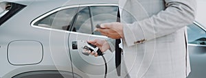 Man holding power supply cable at electric vehicle charging station, closeup