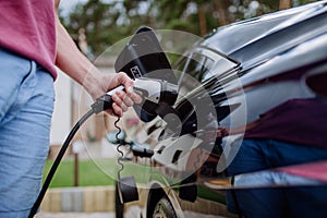 Man holding power supply cable at electric vehicle charging station, closeup