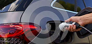 Man holding power supply cable at electric vehicle charging station, closeup