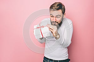 Man is holding a present in his hands. He likes it very much. Isolated on pink background.