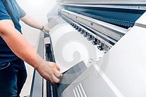 man holding printable material on alarge format printing plotter