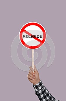 Atheism concept. Man holding prohibition sign with crossed out word Religion on color background