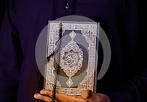 Man Holding Quran. Islamic Background. Arabic on the cover translated with Quran, Muslim man hands holding Quraan with praying photo