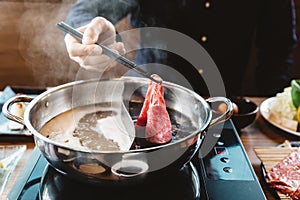 Man holding rare slice Wagyu A5 beef by chopsticks for boiling in Shabu hot pot