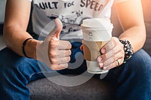 The man holding the recyclable coffee cup and make thumb up