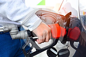 Man holding red fueling nozzle and pumping gasoline fuel fill in car at gas station, car fuels or transportation concept