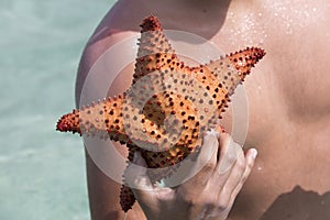 Man holding a red starfish in hand with the odean in the backgro