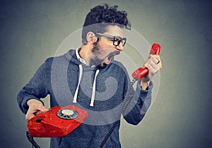 Man holding red telephone receiver and yelling in anger.