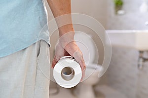 Man holding a roll of tissue in front of the toilet. Man has stomach pain, diarrhea