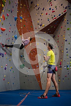 Man holding rope looking at athlete climbing wall in fitness club