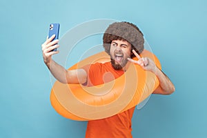 Man holding rubber ring and cell phone, having video call or broadcasting livestrem showing v sign.