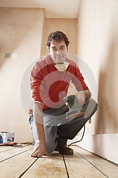 Man Holding Sander While Kneeling In Unrenovated Room photo
