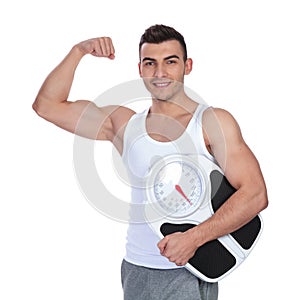 man holding scale and flexing his biceps