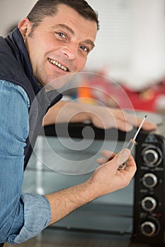 man holding screwdriver next to electric oven photo