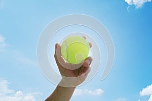 Man holding and serving a yellow tennisball against blue sky. Sports, competition and fitness concept photo