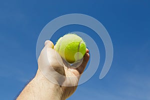 Man holding and serving a yellow tennisball against blue sky. Sports, competition and fitness concept photo