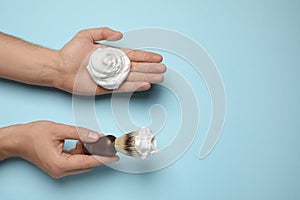 Man holding shaving foam and brush on light blue background, top view. Space for text