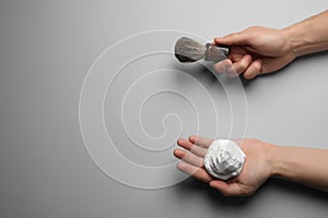 Man holding shaving foam and brush on light grey background, top view. Space for text