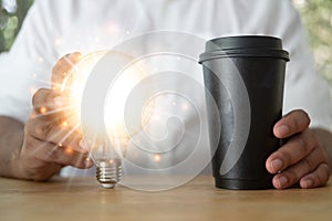 Man holding a shining light bulb and holding a cup of hot coffee. Idea and innovation concept