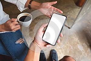 a man holding and showing mobile phone with blank desktop screen to his friend while having conversation together