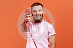 Man holding and showing retro phone handset to camera, asking to answer phone.