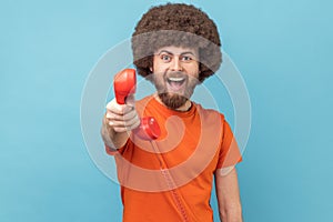 Man holding and showing retro phone handset to camera, asking to answer phone.