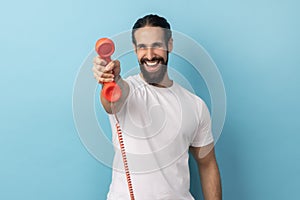 Man holding and showing retro phone handset to camera, asking to answer phone.