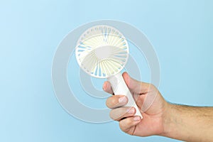 Man holding small portable usb fan close-up isolated on blue background