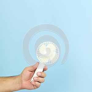 Man holding small portable usb fan close-up isolated on blue background