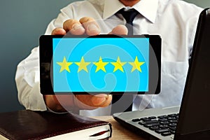 Man holding smartphone with five stars rating. Customer satisfaction.