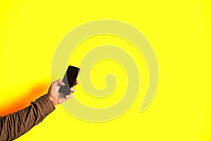 Man is holding smartphone in hands isolated on yellow background. Addicted to technologies