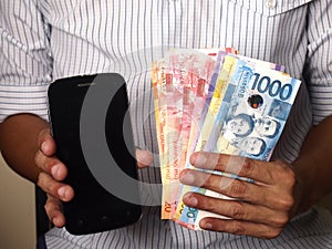 Man holding a smartphone and Philippine peso bills