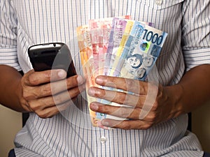 Man holding a smartphone and Philippine peso bills