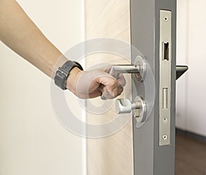 Man holding stainless steel door handle on a wooden door to open and show a part of door Latch