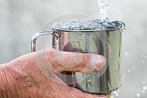 Man is holding a steel mug and a well water is pouring from a bucket