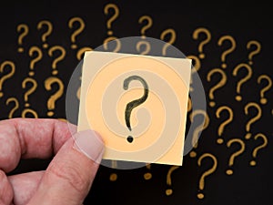 A man holding a sticky note with a question mark on it in his hand against a question mark background