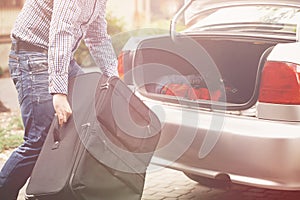 Man holding suitcase in front of open car trunk