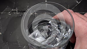 Man holding; swirling alcohol with ice cubes; slow motion; black wrinkled shabby crumpled paper background.