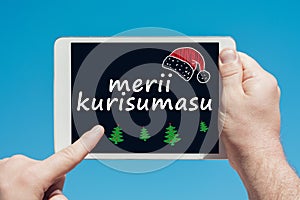 Man holding a tablet device with text in japanese `Merii Kurisumasu` Merry Christmas