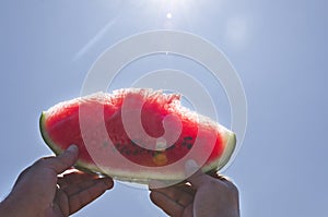 Man holding tasty sweet slice of watermelon against blue summer sky