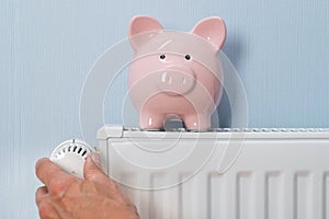 Man holding thermostat with piggy bank on radiator