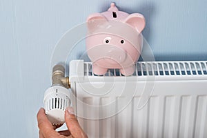 Man holding thermostat with piggy bank on radiator