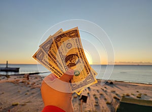 A man holding three one-dollar banknotes in his hand against backdrop of the sea photo