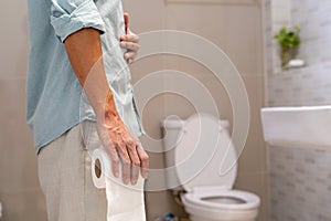 Man holding tissue paper roll standing in front of toilet. Men have abdominal, diarrhea or waist pain. Stomach health problem